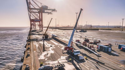 Schwertransport von Windradflügeln mit Kränen am Hafen bei Sonnenuntergang